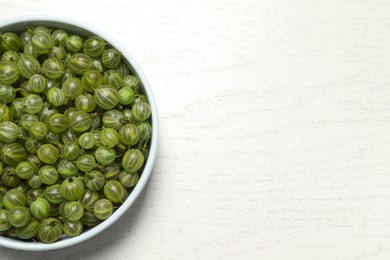 Photo of Bowl of fresh ripe gooseberries on white wooden table, top view. Space for text