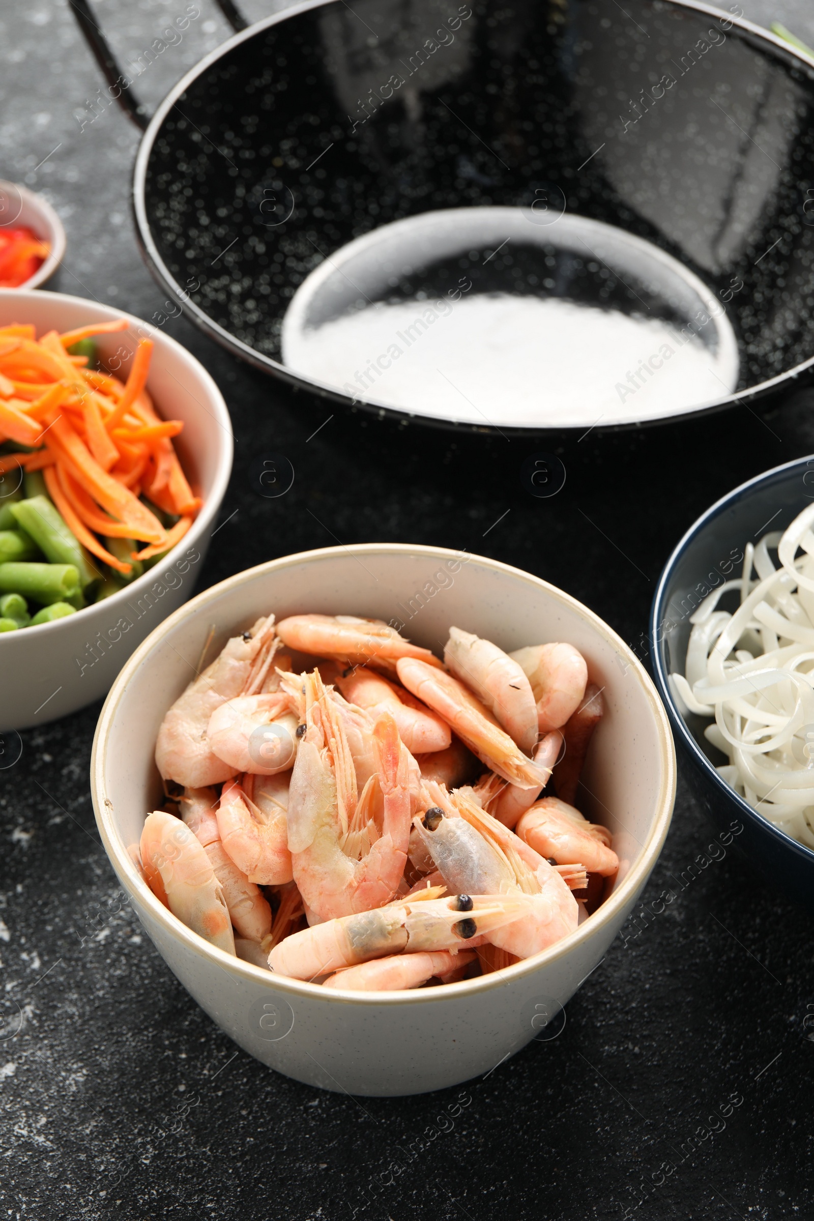 Photo of Shrimps, vegetables and black wok on grey textured table, closeup