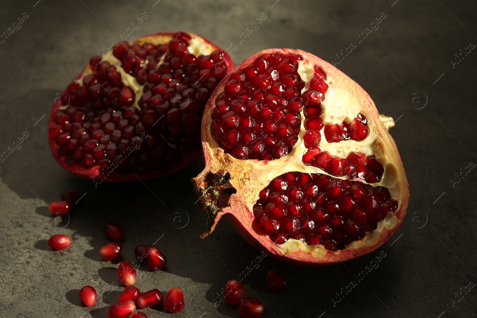 Photo of Pieces of ripe juicy red pomegranate with grains on grey textured table, closeup