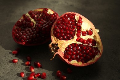 Photo of Pieces of ripe juicy red pomegranate with grains on grey textured table, closeup