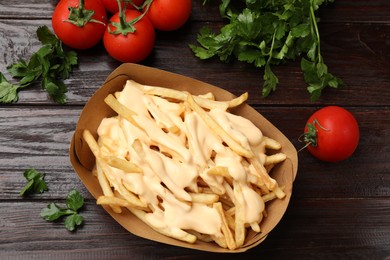 Tasty potato fries, cheese sauce in paper container and products on wooden table, top view