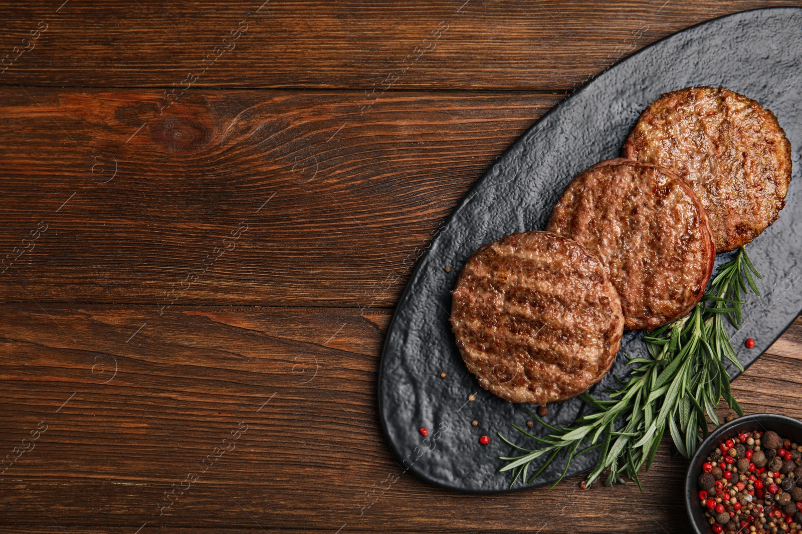 Photo of Slate plate with tasty grilled hamburger patties and seasonings on wooden table, flat lay. Space for text