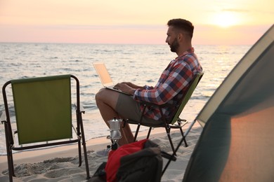 Man using laptop in camping chair on sandy beach