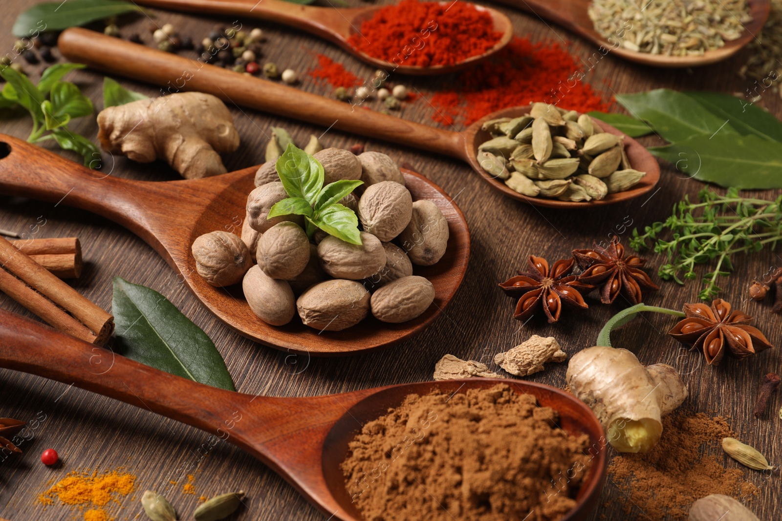 Photo of Different herbs and spices with spoons on wooden table, closeup