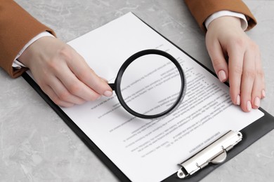 Woman looking at document through magnifier at light gray table, closeup. Searching concept