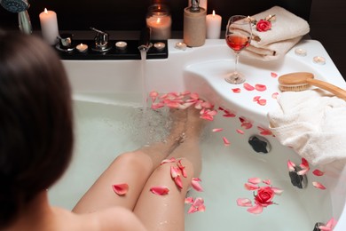 Photo of Woman taking bath with rose petals, closeup. Romantic atmosphere