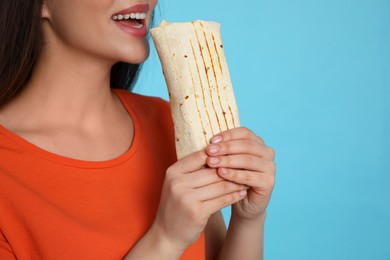 Young woman eating tasty shawarma on turquoise background, closeup