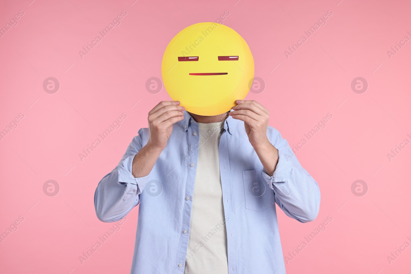 Photo of Man holding emoticon with closed eyes and mouth on pink background