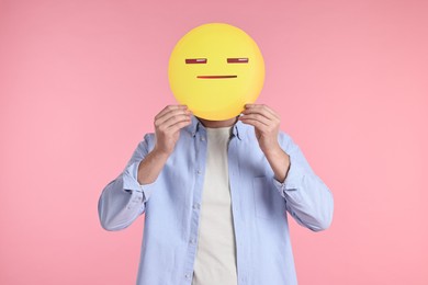 Photo of Man holding emoticon with closed eyes and mouth on pink background