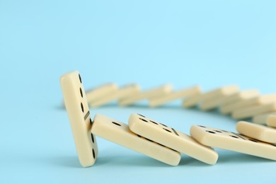 Photo of White domino tiles falling on light blue background. Space for text