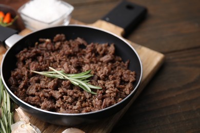 Photo of Fried ground meat in frying pan and rosemary on wooden table, closeup. Space for text