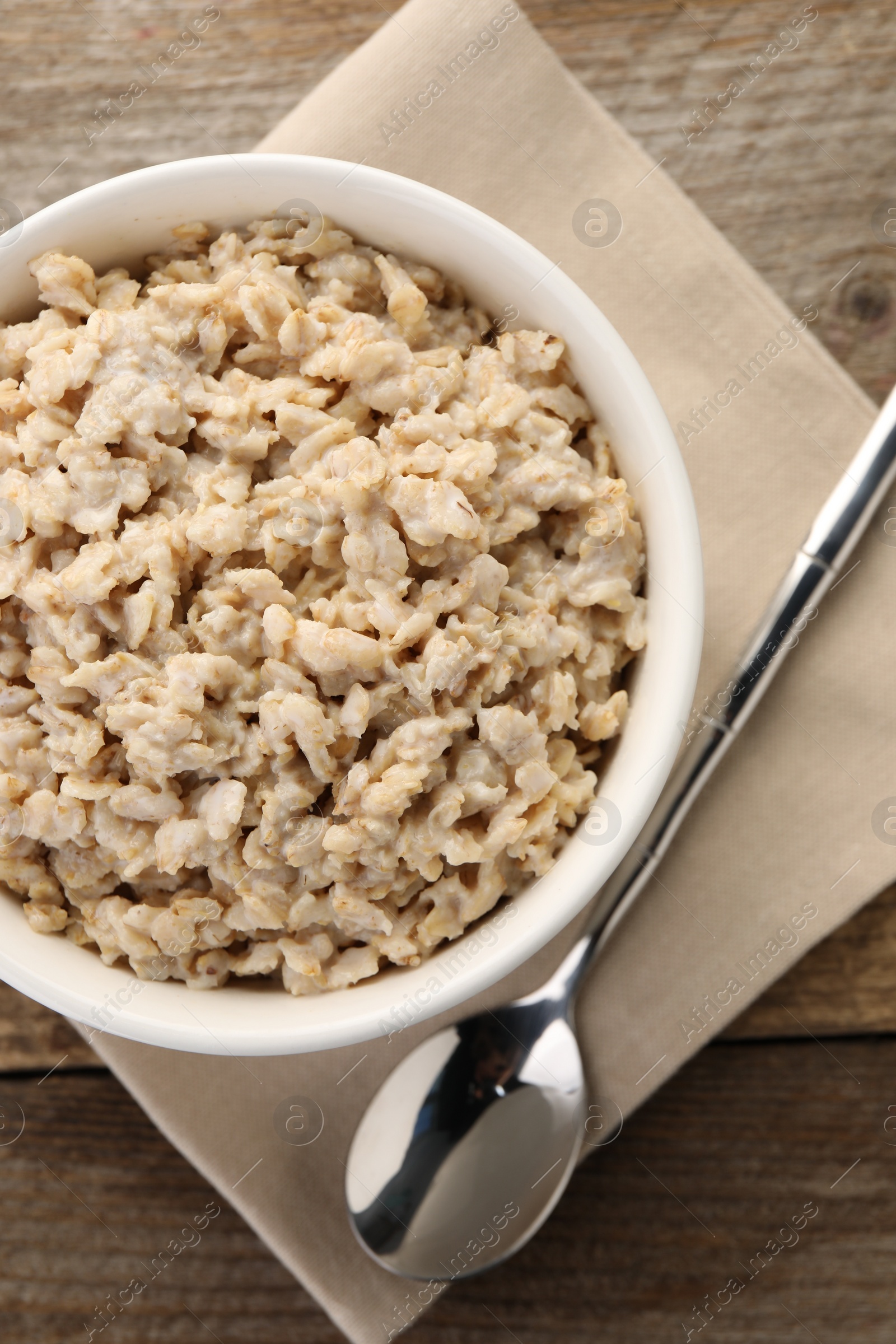 Photo of Tasty boiled oatmeal in bowl and spoon on wooden table, top view