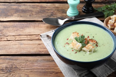 Delicious asparagus soup with croutons served on wooden table, space for text