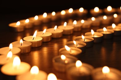 Photo of Burning candles on wooden table in darkness, closeup