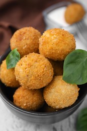 Photo of Bowl of delicious fried tofu balls with basil on textured table, closeup