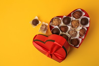 Photo of Heart shaped box with delicious chocolate candies on yellow background, flat lay. Space for text