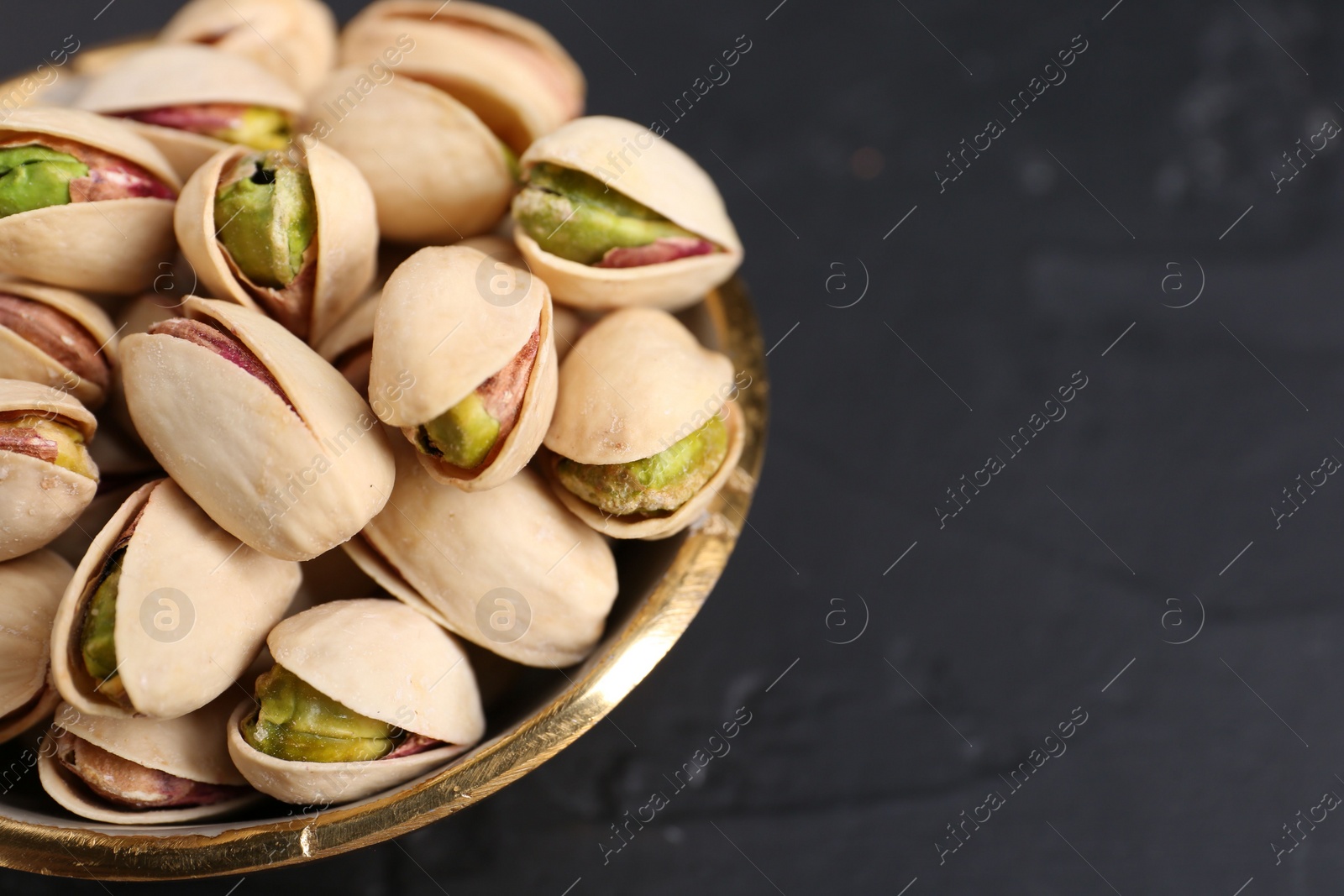 Photo of Tasty pistachios in bowl on black table, closeup. Space for text