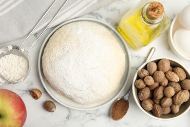 Photo of Raw dough, nutmeg seeds and other ingredients for pastry on white marble table, flat lay