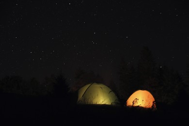 Photo of Camping tents glowing at night outdoors. Space for text