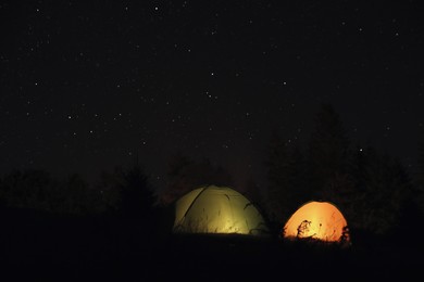 Camping tents glowing at night outdoors. Space for text