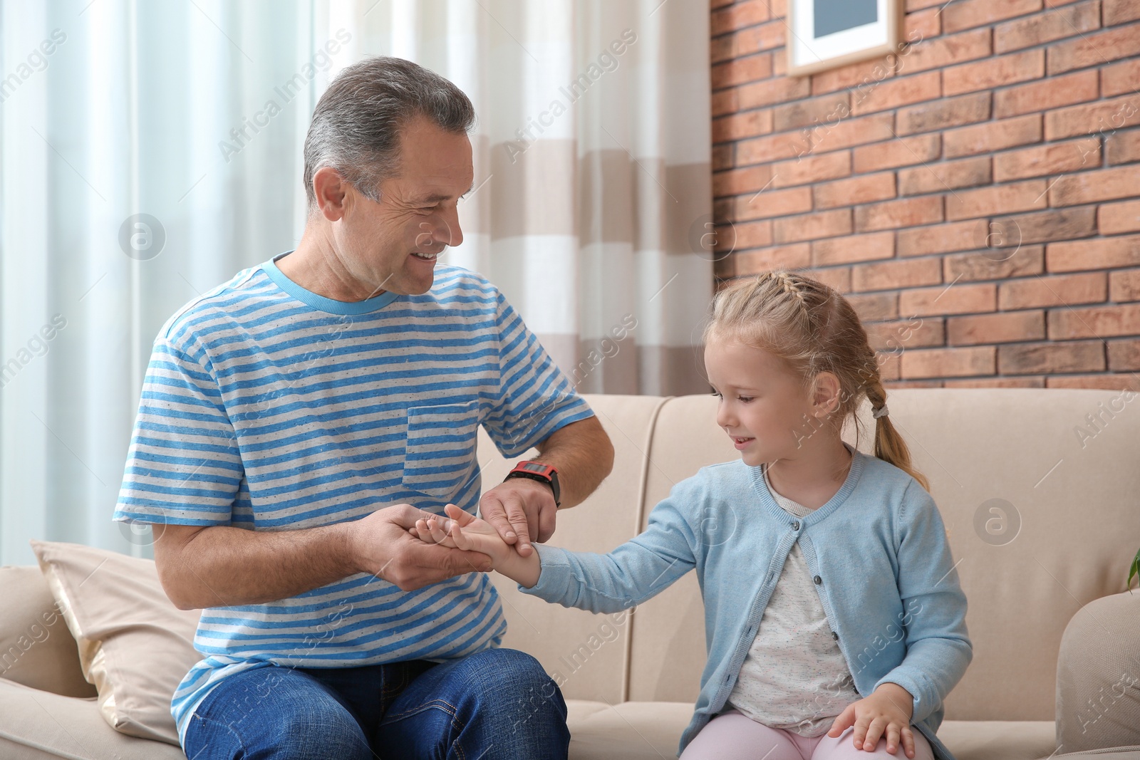 Photo of Mature man checking little girl's pulse with fingers at home