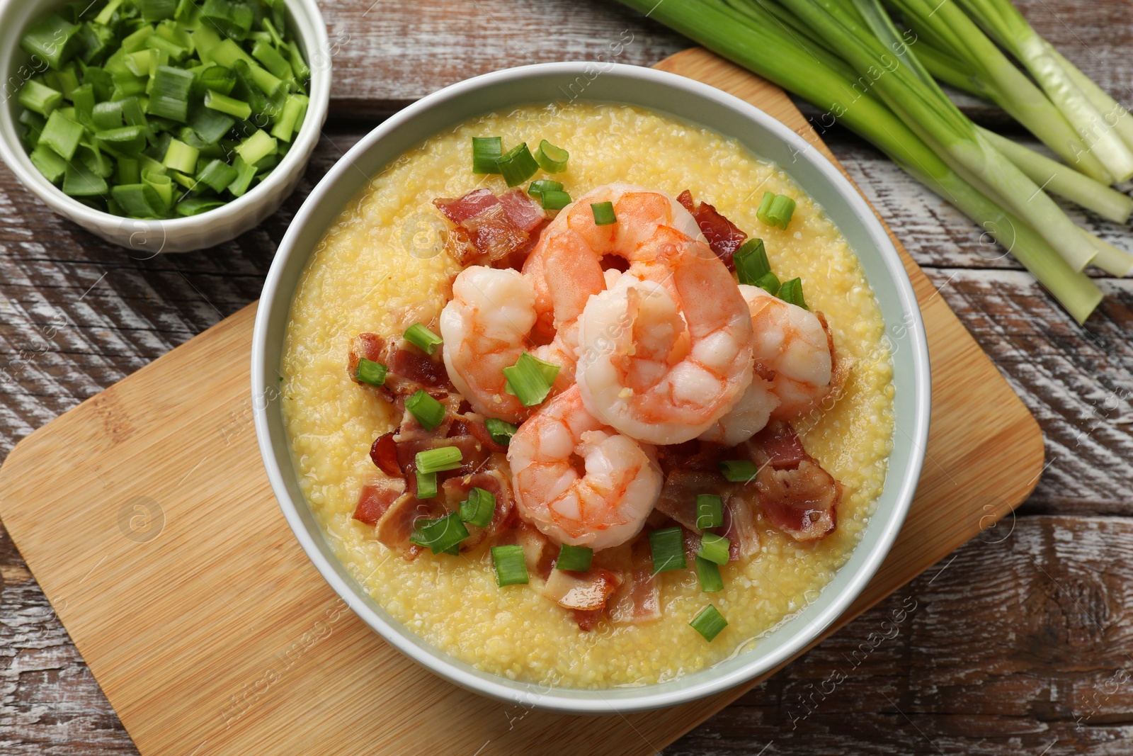 Photo of Fresh tasty shrimps, bacon, grits and green onion in bowl on wooden table, flat lay