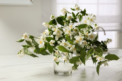 Bouquet of beautiful jasmine flowers in glass vase on white marble table indoors