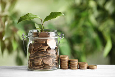 Coins and green sprout on white wooden table against blurred background. Money savings