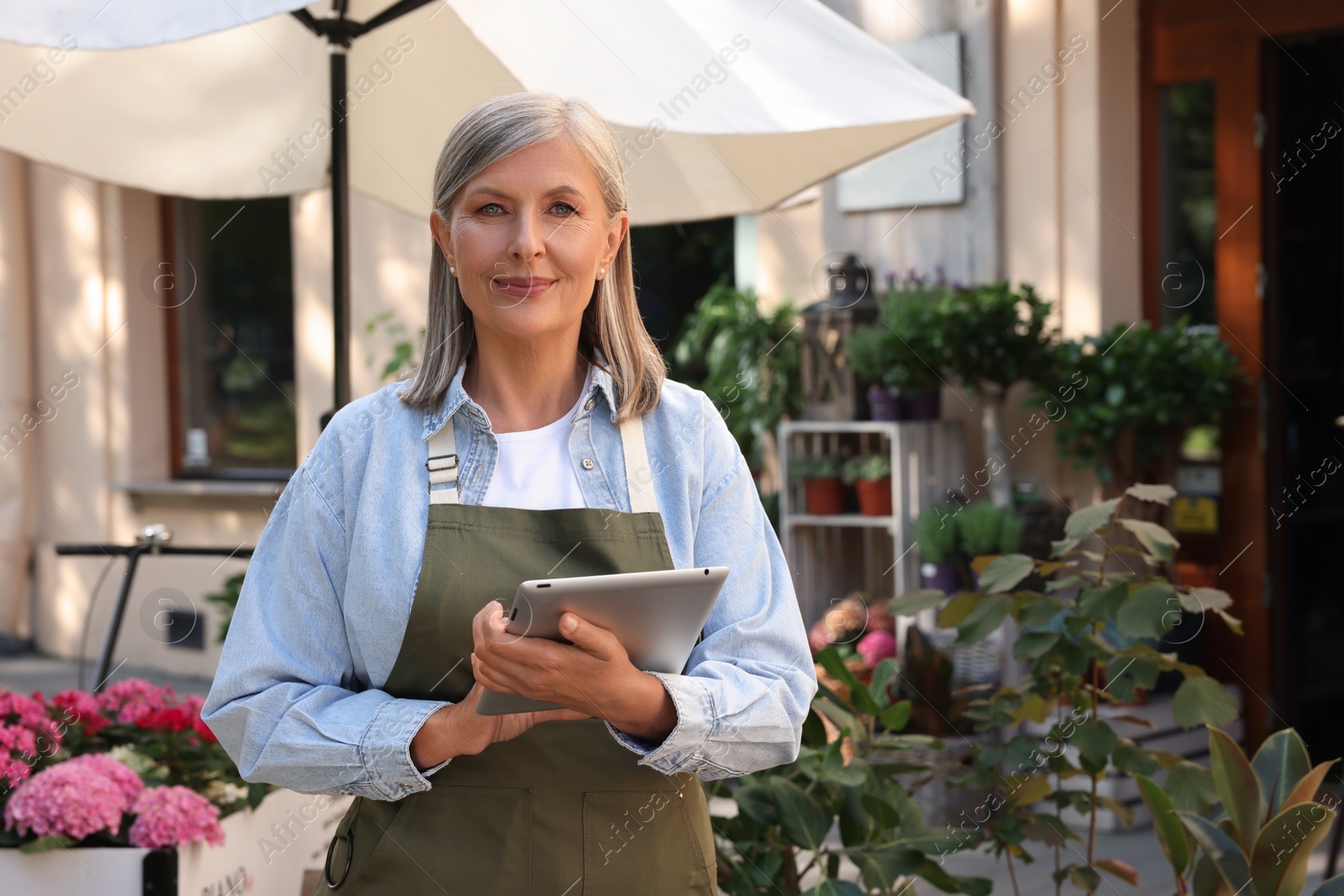 Photo of Smiling business owner with tablet near her flower shop outdoors, space for text