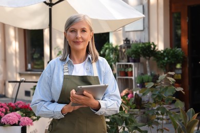 Photo of Smiling business owner with tablet near her flower shop outdoors, space for text