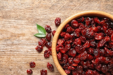 Photo of Bowl with cranberries on wooden background, top view with space for text. Dried fruit as healthy snack