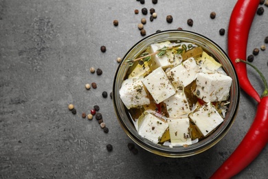 Flat lay composition with feta cheese marinated in oil on grey table, space for text. Pickled food