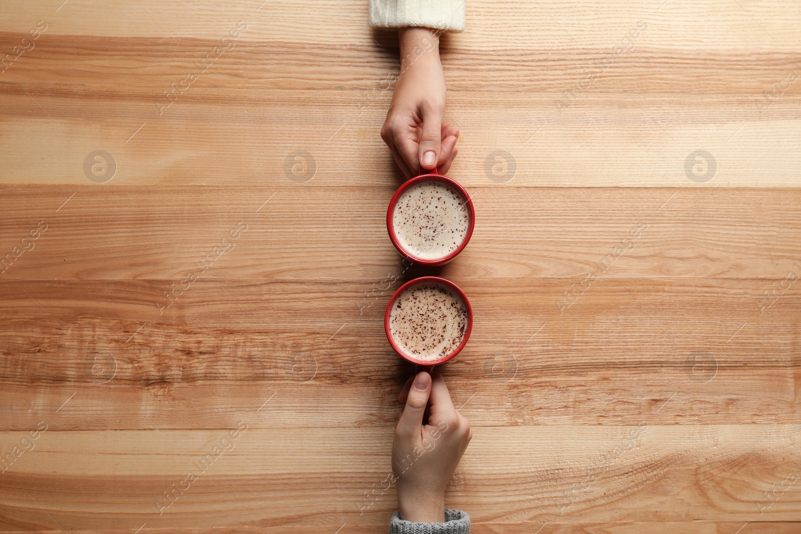 Photo of Women with cups of coffee at wooden table, top view