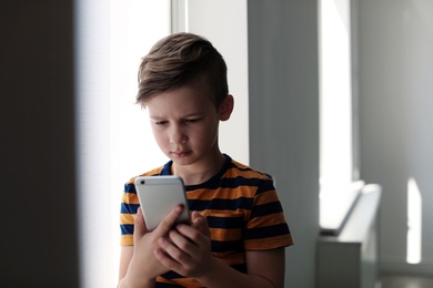 Photo of Sad little child with smartphone indoors. Danger of internet