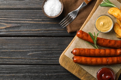 Photo of Flat lay composition with delicious grilled sausages on dark wooden table, space for text. Barbecue food