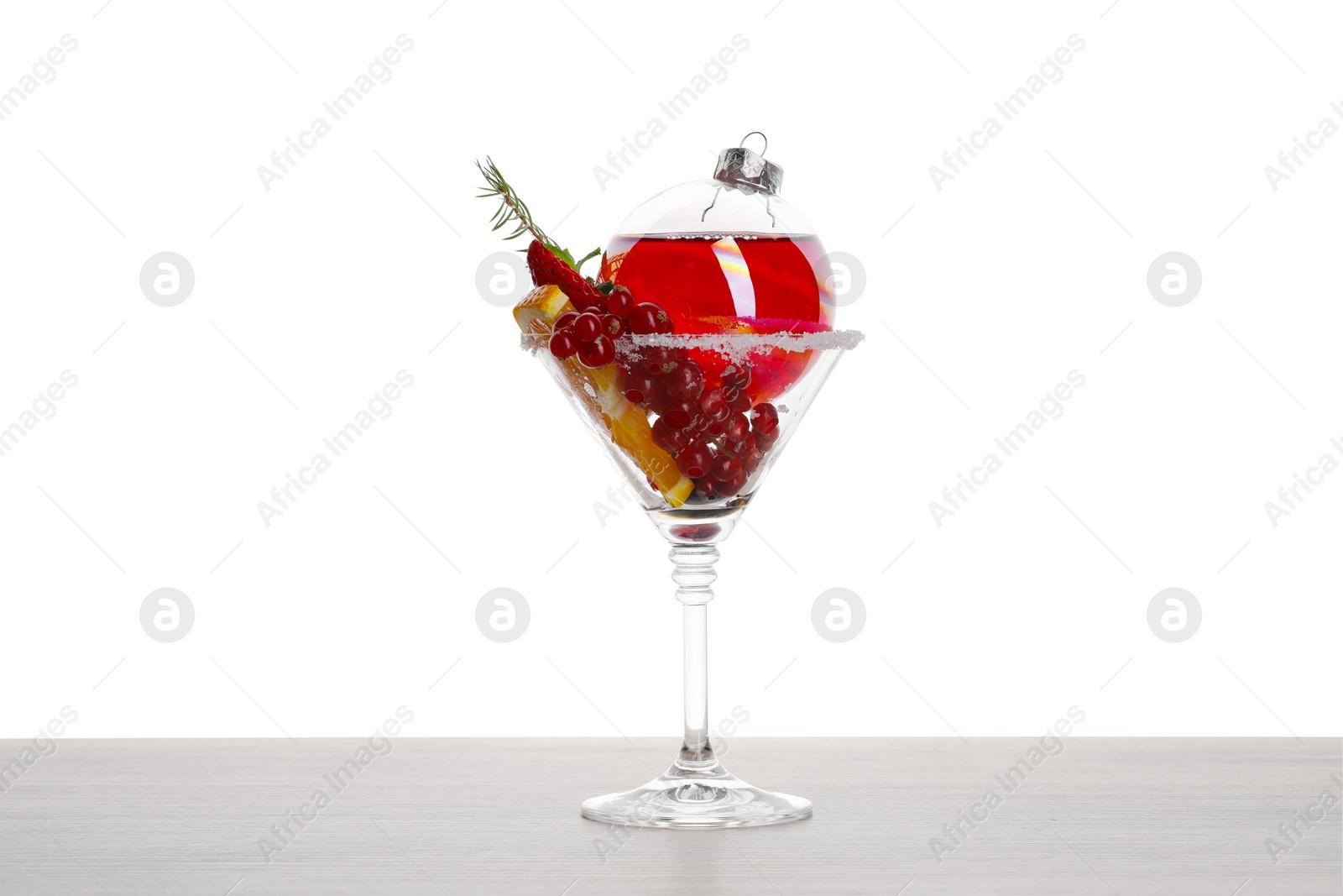 Photo of Creative presentation of Christmas Sangria cocktail in bauble and glass on light wooden table against white background