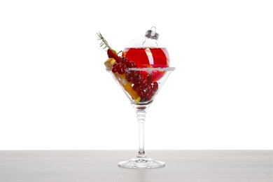 Photo of Creative presentation of Christmas Sangria cocktail in bauble and glass on light wooden table against white background