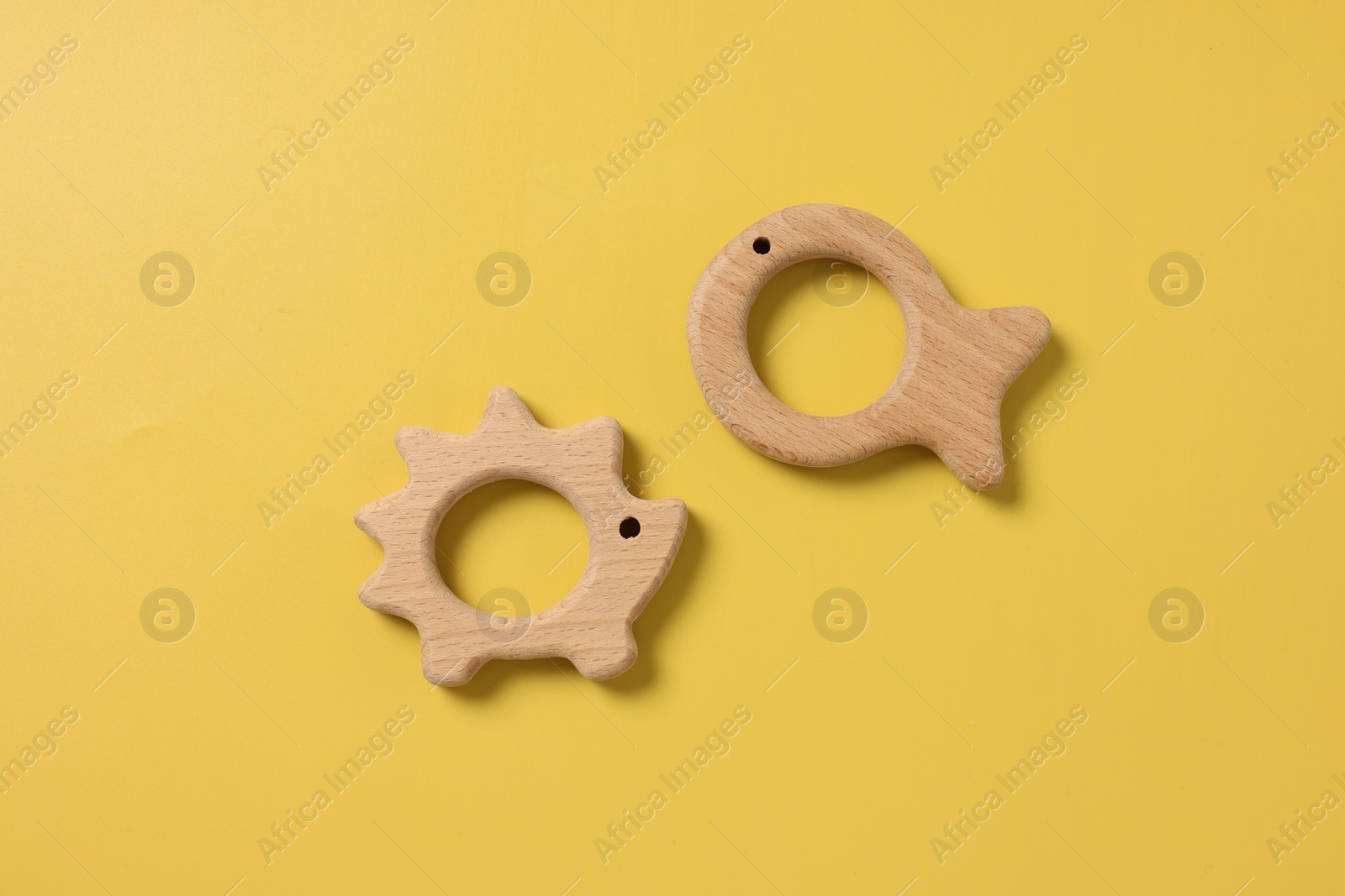 Photo of Baby accessories. Wooden teethers on yellow background, top view