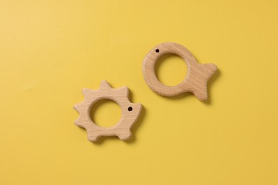 Baby accessories. Wooden teethers on yellow background, top view