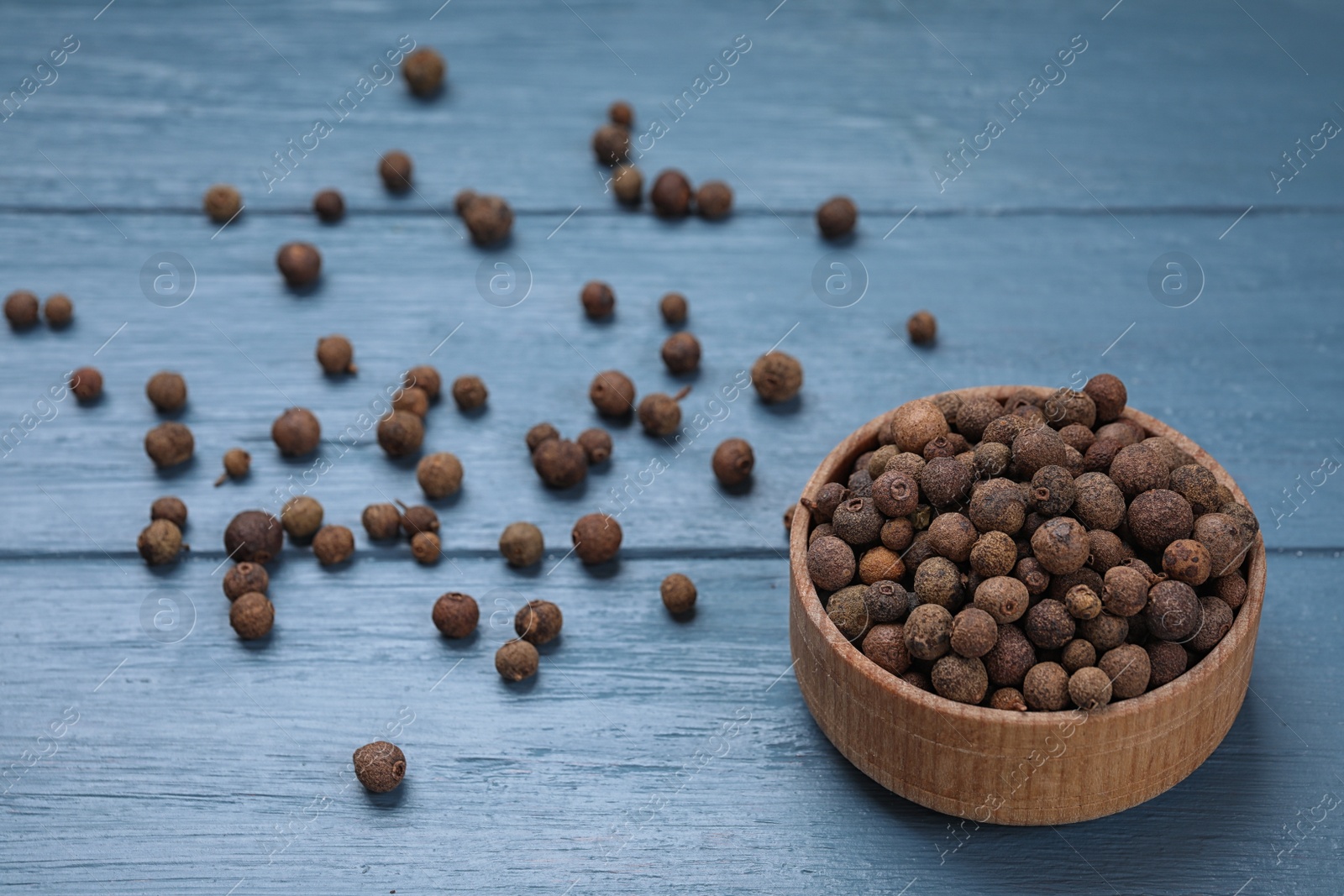 Photo of Black peppercorns in bowl on blue wooden table