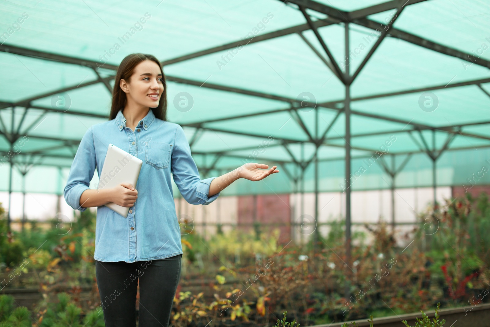 Photo of Female business owner with tablet showing her greenhouse. Space for text