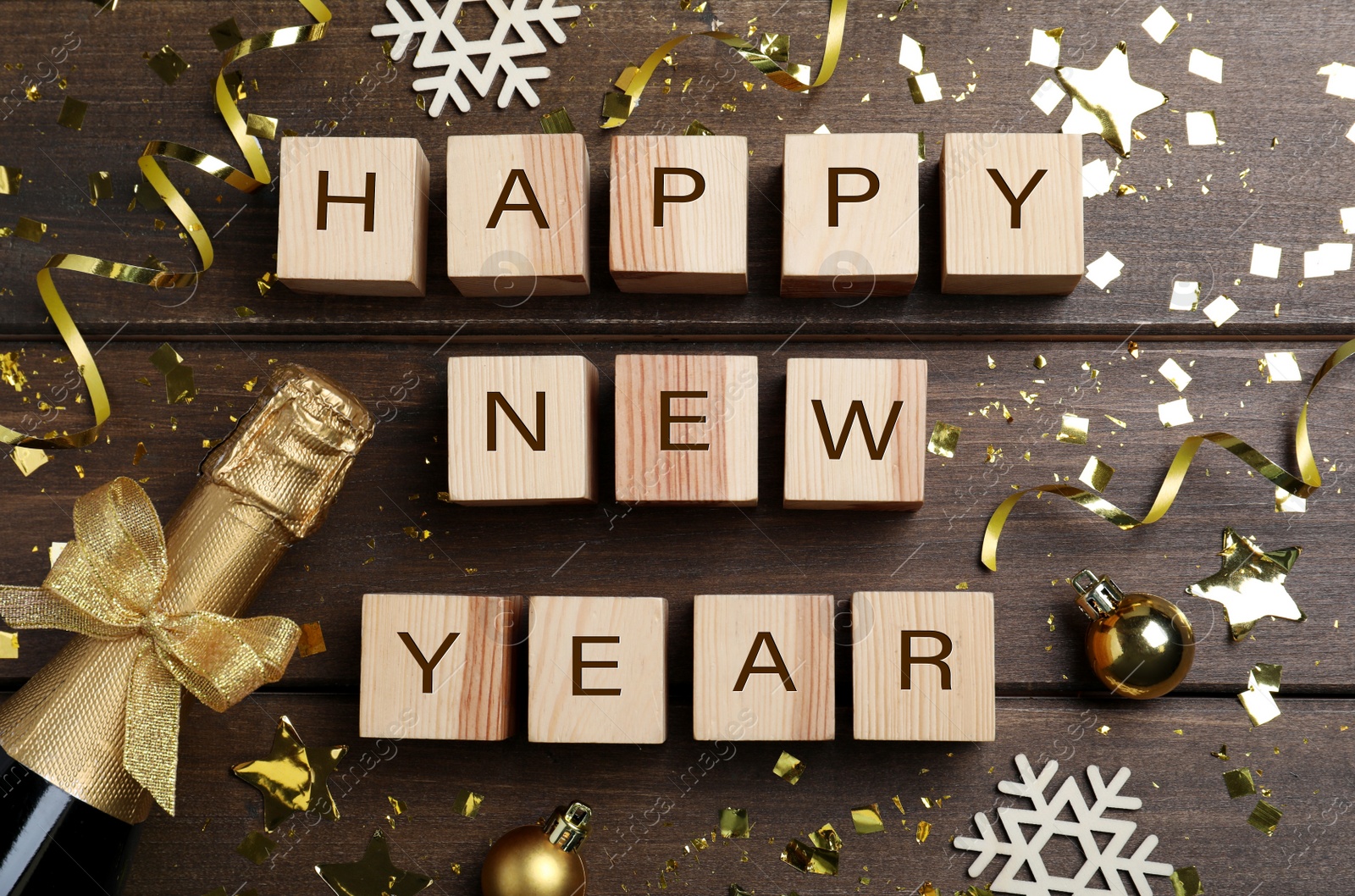 Photo of Phrase Happy New Year made of cubes, sparkling wine and festive decor on wooden background, flat lay