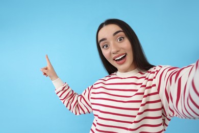 Photo of Surprised young woman taking selfie on light blue background
