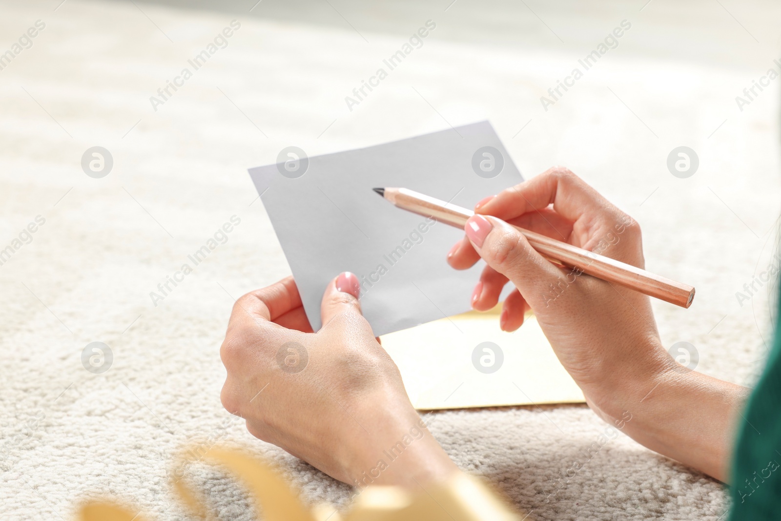 Photo of Woman writing message in greeting card on carpet in room, closeup