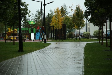 Photo of City street with colorful playground and puddles on pavement after rain outdoors