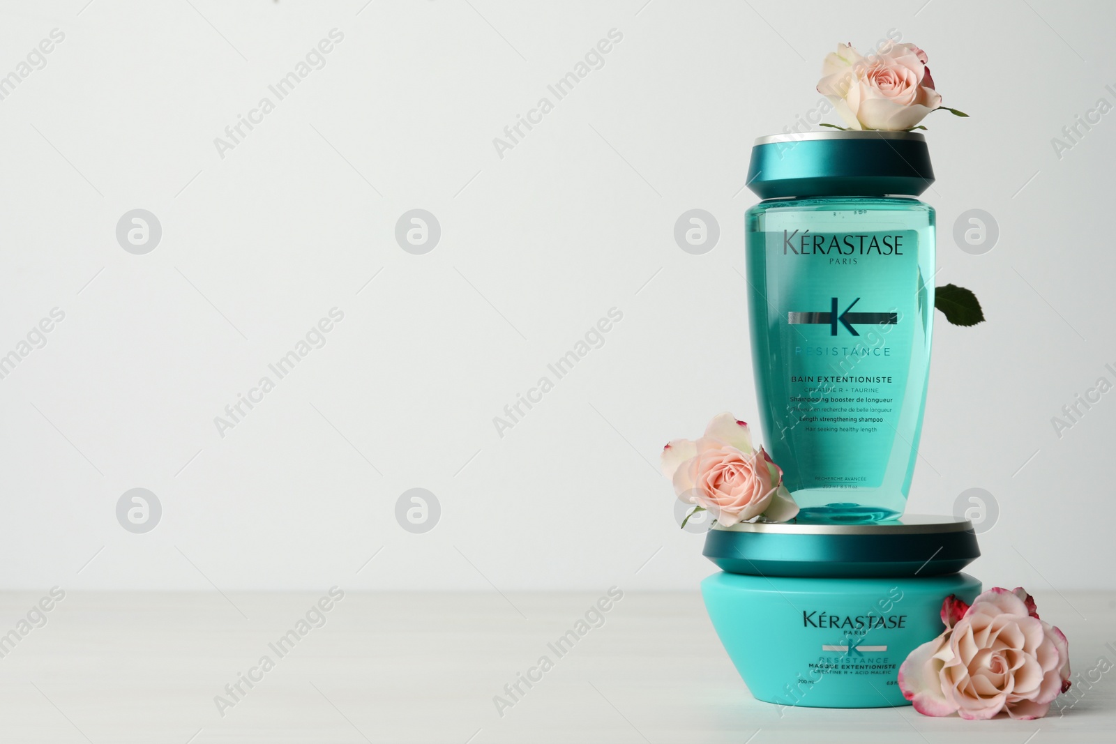 Photo of MYKOLAIV, UKRAINE - SEPTEMBER 07, 2021: Kerastase hair care cosmetic products and beautiful flowers on white wooden table. Space for text