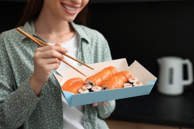 Photo of Woman eating sushi rolls with chopsticks in kitchen, closeup