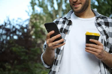 Photo of Young man with smartphone and cup of coffee in park, closeup