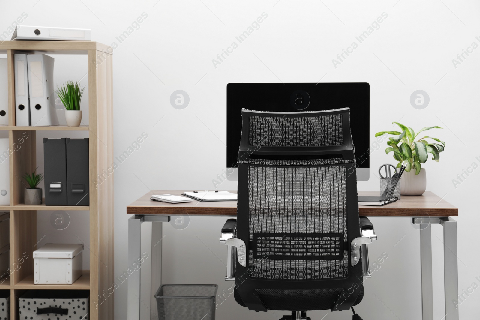 Photo of Cozy workspace with computer on desk, chair and bookcase near white wall at home