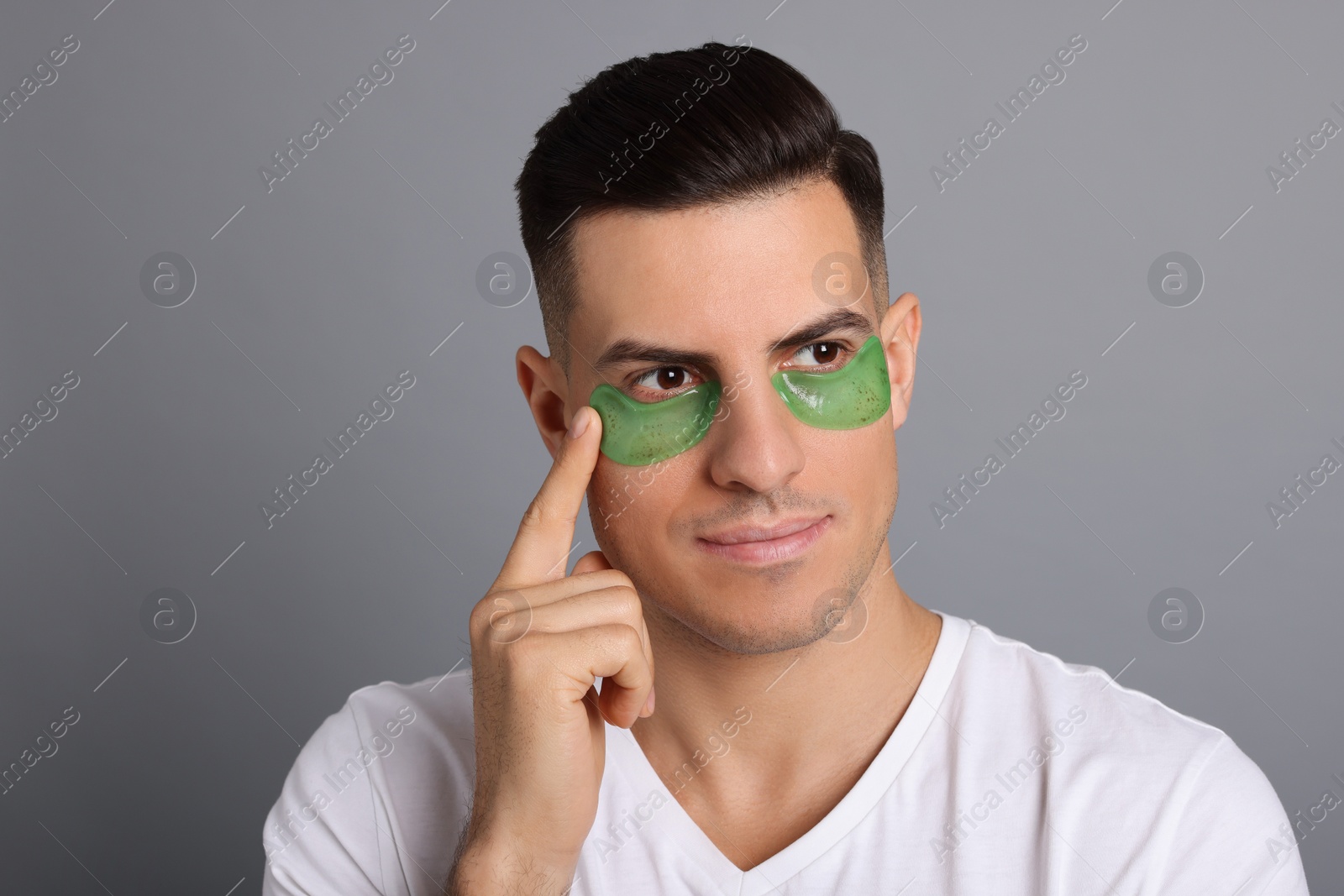 Photo of Man applying green under eye patch on grey background